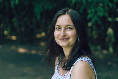 Genç, güzel esmer kız yaz günü parkta gülümsüyor.