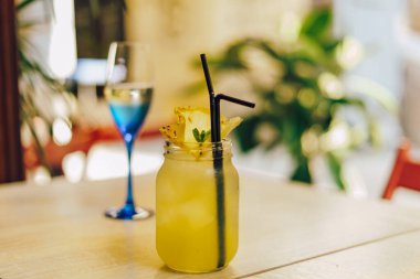 Masada bir bardak beyaz şarap ve sarı kokteyl. Lezzetli ananas kokteyli.