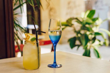 Masada bir bardak beyaz şarap ve sarı kokteyl. Lezzetli ananas kokteyli.