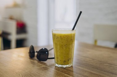 Masada bir bardak sarı smoothie var. Bir bardak smoothie ve güneş gözlüğü.