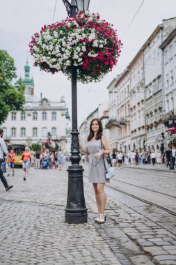 Şehirde çiçeklerin arka planında esmer bir kız. Şehir merkezinde güzel yaz çiçekleri olan bir sütun. Şehrin arka planında pembe, kırmızı ve beyaz çiçeklerin çiçek manzarası.