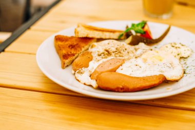 Beyaz tabakta iştah açıcı bir kahvaltı. Bir kafede çırpılmış yumurta, sebze ve kızarmış ekmek. Kafede kahvaltı: omlet, sosis ve tost.