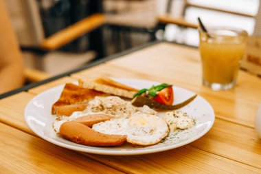 Kafede nefis bir kahvaltı: çırpılmış yumurta ve bir bardak meyve suyu. Sosisli, domatesli ve peynirli omlet. Jambonlu omlet ve beyaz yuvarlak tabakta tost.