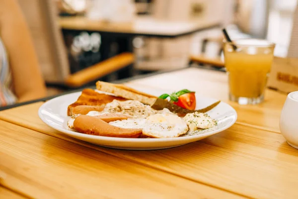 Kafede nefis bir kahvaltı: çırpılmış yumurta ve bir bardak meyve suyu. Sosisli, domatesli ve peynirli omlet. Jambonlu omlet ve beyaz yuvarlak tabakta tost.