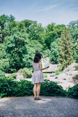 Sofia Park, Ukrayna. Güzel bir yaz parkında genç bir kız. Üzerinde turist haritası olan renkli elbiseli bir kız. Parktaki gözlem güvertesinde elinde turist haritası olan bir kadın.