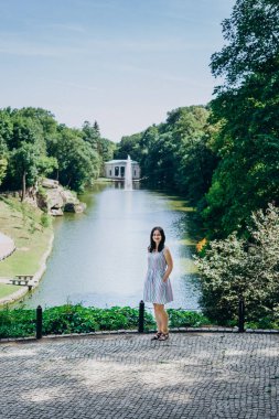 Sofia Park, Ukrayna. Peyzaj parkındaki esmer kız. Güzel bir parkta fıskiyenin arka planındaki kız. Gölün yanında beyaz bir çardağı olan çeşme.