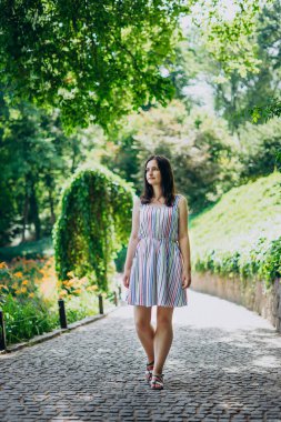 Sofia Park, Uman. Kız güneşli bir günde parkın ara sokaklarında yürür. Beyaz elbiseli esmer kız güzel bir manzara parkında yürüyor. Güzel yeşil bir parkta kaldırım taşlarıyla dolu bir yol.