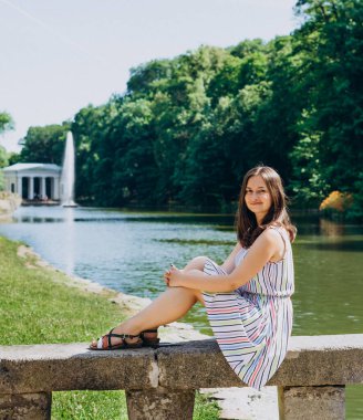 Sofia Park, Uman. Gölün arka planındaki bankta oturan genç bir kadın. Elbiseli kız taş bir bankta oturuyor..