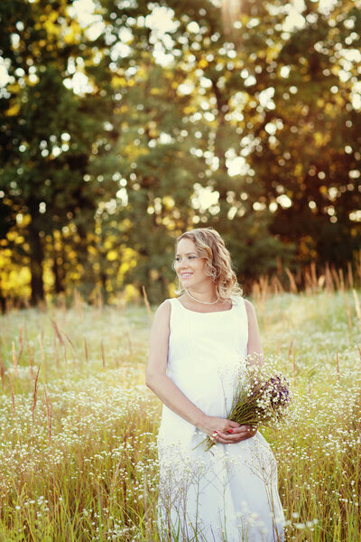 Pregnant woman in summer field with with a bouquet of wildflowers