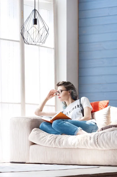Unga smart kvinnlig student studera flitigt hemma nära stora fönster. Balkong, soffa, mjuka kuddar. — Stockfoto