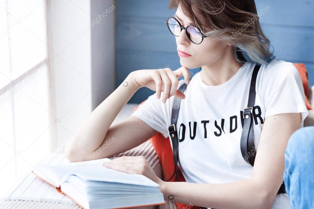 Young smart female student studying diligently at home near large window. Sunny day, sofa, soft pillows