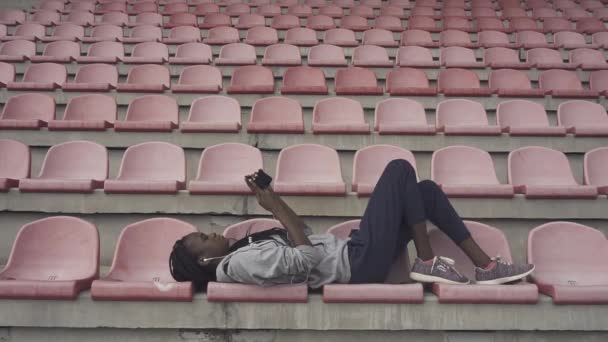 Atletisk afroamerikanska flicka resten av hård träning liggande på stolarna och surfa på internet — Stockvideo