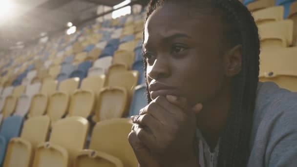 Retrato de cerca de una joven mujer afroamericana sentada en el estadio y fijamente buscando algo — Vídeos de Stock