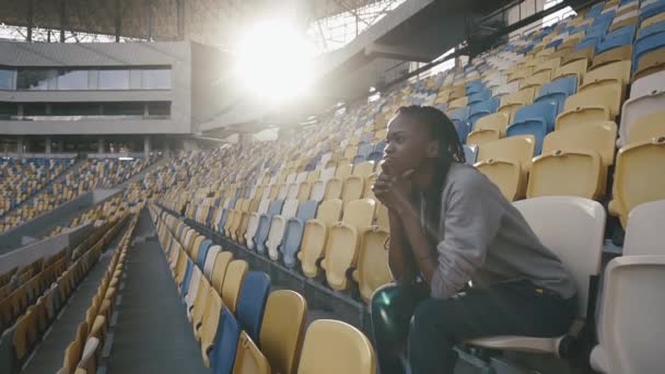 Portret van jonge african american vrouw die aan het stadion zit trainen en vastgezet op zoek naar iets — Stockvideo