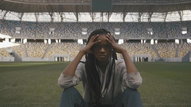 Нервова спортивна афро-американська жінка сидить на самоті в центрі спортивного стадіону Ог і дивиться в камеру — стокове відео