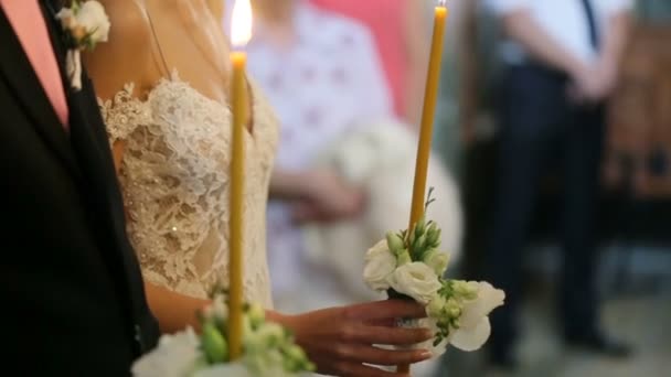 Esküvői pár tart sárga gyertyák, a fehér virágok a templomban ünnepségen — Stock videók