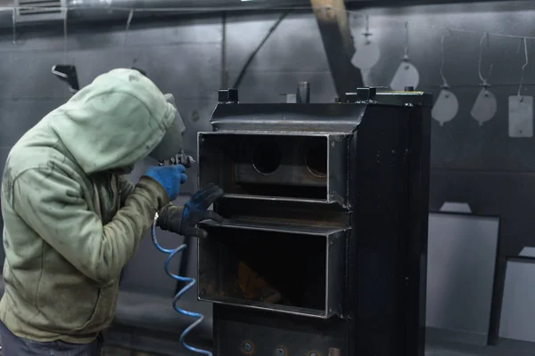Worker sprays black paint on solid fuel boiler