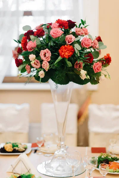 Rich green bouquet with red roses stands in glass vase