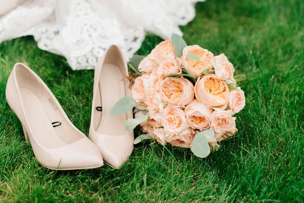 Beautiful peach bouquet lies by beige wedding shoes