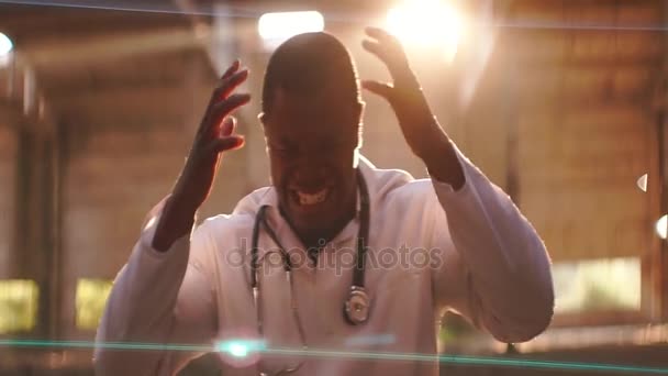 Strong angry black man standing on the light of sunset, sunrise, taking up and squeezing his hands,tackle his head, compressing the teeth, screaming, anamorphic lense — Stock Video