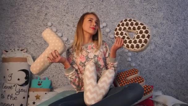 Mooi meisje zittend op bed in kamer spelen met decoratieve kussens — Stockvideo