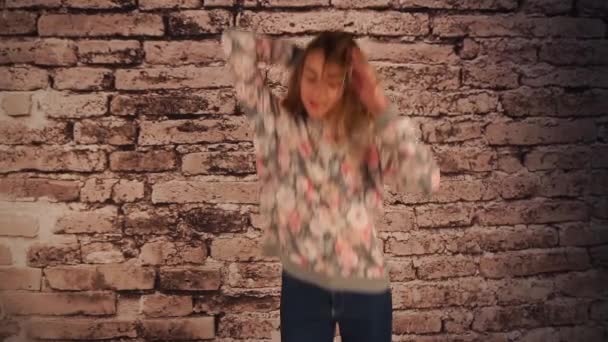 Hermosa chica de pie cerca de la pared, saltando, bailando y jugando con el pelo, agitando la cabeza — Vídeos de Stock