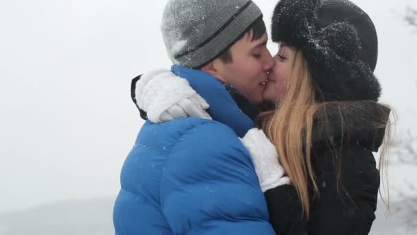 Молодая счастливая пара целуется в зимнем снежном лесу — стоковое видео