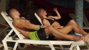 Çift havuz yakınındaki şezlong üzerinde sohbet. güzel erkek ve kadın gülüyor ve sohbet.