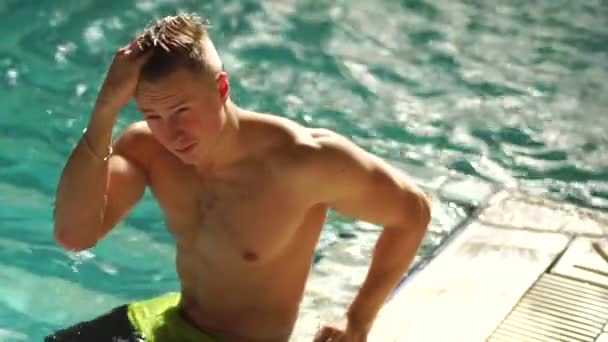 Ein Mann mit nacktem Oberkörper sitzt im Pool. Kerl nimmt seine Hand zum Kopf und korrigiert die Haare. — Stockvideo