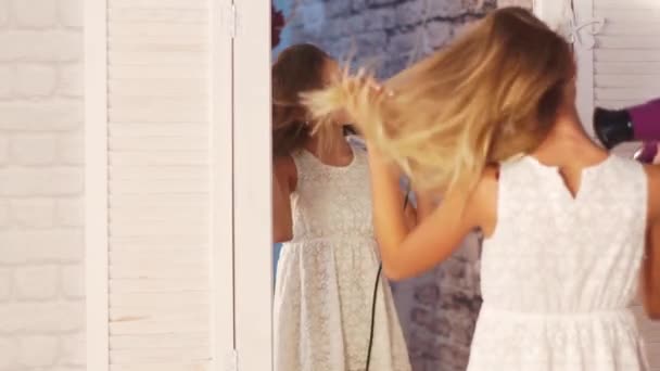 Дівчина-підліток у білій сукні танцює перед дзеркалом шафи з фену в руках, співає і посміхається  . — стокове відео