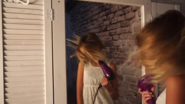 Tienermeisje in witte jurk is dansen voor de garderobe spiegel met föhn in haar handen, zingen en glimlachend schudt haar hoofd — Stockvideo