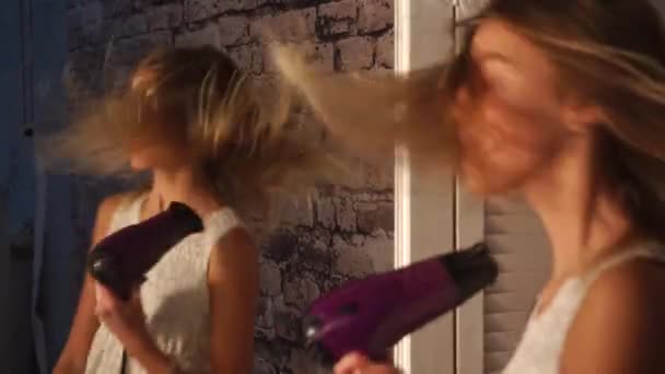 Young girl in dress is dancing in front of the wardrobe mirror with hair dryer in her hands, smiling, singing, looking at face and shaking her head. — Stock Video