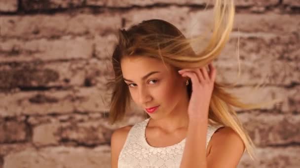 Ein junges Mädchen im Teenageralter steht in der Nähe der Mauer, schüttelt den Kopf, spielt mit den Haaren und blickt in die Kamera. der Wind bläst und ihr Haar flattert. — Stockvideo