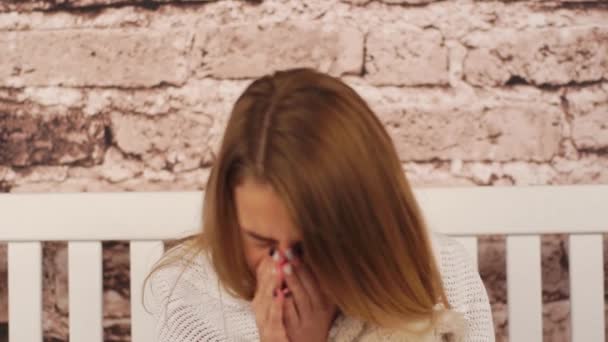 Young teenage girl feeling sick. She sitting on the bench, hugging a teddy bear and sneezing. Her sore is throat. Covered her shoulders with white coverlid. — Stock Video