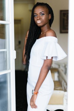 lüks otel odasında açık kapı önünde duran beyaz uzun elbiseli güzel siyah modeli. güneşe bakıyor