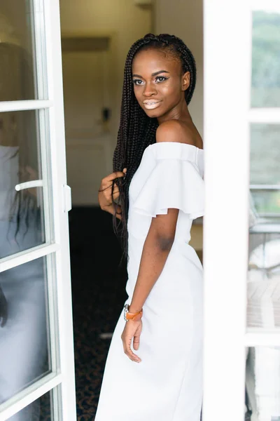 Bela menina africana em pé na frente da porta aberta.corpo é refletido no vidro. Modelo em vestido branco . — Fotografia de Stock