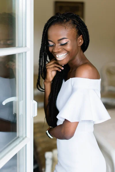 Aantrekkelijke Afrikaanse vrouw staan voor de deur open in de VIP-luxe hotelkamer en glimlachen. Ze is het dragen van witte elegante jurk. mooie glimlach, gelukkig emoties — Stockfoto
