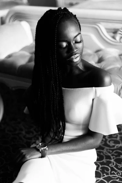 Foto em preto e branco de uma mulher africana incrível sentada no chão em um hotel europeu vip. Quarto de hotel com interior clássico — Fotografia de Stock