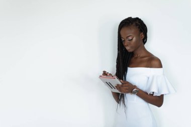 Siyah deri ile model beyaz bir duvarın önünde duran ve onun tablet kullanarak Internet sohbet. Kız çıplak omuz ile beyaz elbise giyiyor.