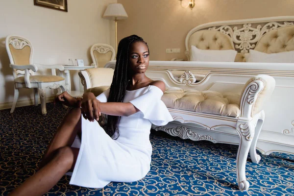 Привлекательная африканская женщина в роскошном европейском отеле. Модель, сидящая на полу, покрытая синим ковром. Она положила руки на колено. Номер оформлен в классическом стиле . — стоковое фото