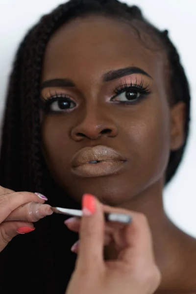 Schattige, sexy, mooie foto-model voorbereiding aan mode schieten. Make-up artiest is het nemen van een bruin lipstick aan haar lippen met behulp van een profesional onbezonnen. — Stockfoto