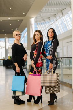 Üç kadın büyük alışveriş merkezinde alışveriş sonra memnun oldum. Milano ile elbise giyen kadın hortumlar ve ellerinde birçok alışveriş torbaları.