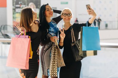 Çekici güzel kadınlar alışveriş sonra selfie alarak. Kızlar çok gülümseyen mutluyuz. Fotoğraflar için poz. Birçok renkli alışveriş torbaları elimde