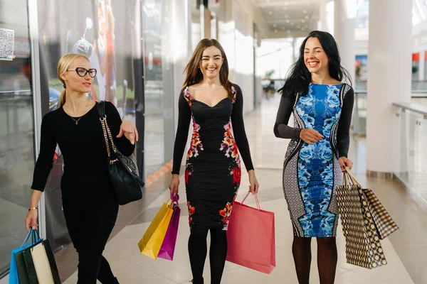 Три зачарованих привабливих жінки мають покупки у великому торговому центрі. Жінка носить сукні з рукавами і має торговельні сумки в руках. Вони дуже щасливі . — стокове фото