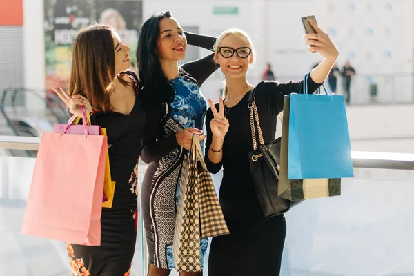 Çekici güzel kadınlar alışveriş sonra selfie alarak. Kızlar çok gülümseyen mutluyuz. Fotoğraflar için poz. Birçok renkli alışveriş torbaları elimde