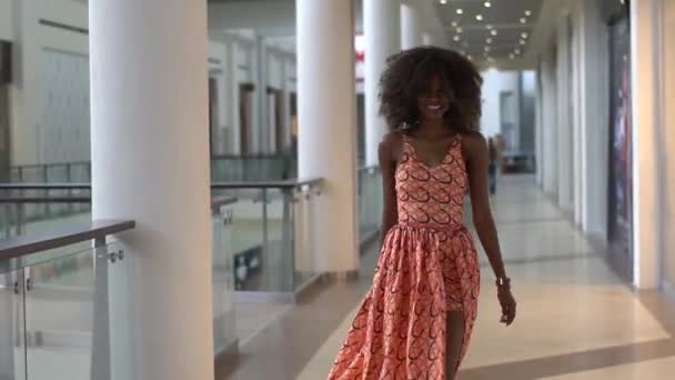 Jovem menina afro-americana sexy andando no vestido laranja brilhante no centro de comércio, girando e olhando para trás — Vídeo de Stock