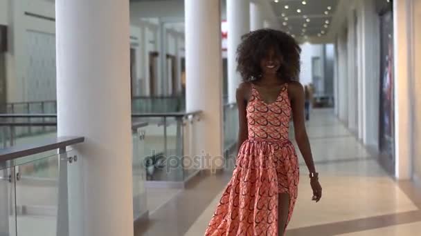 Jeune fille afro-américaine sexy marchant dans la robe orange vif dans le centre commercial, tournant et regardant en arrière — Video