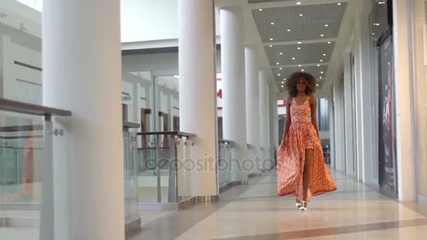 Молода афроамериканська дівчина гуляє в універмазі в помаранчевій сукні і показує своє щастя — стокове відео