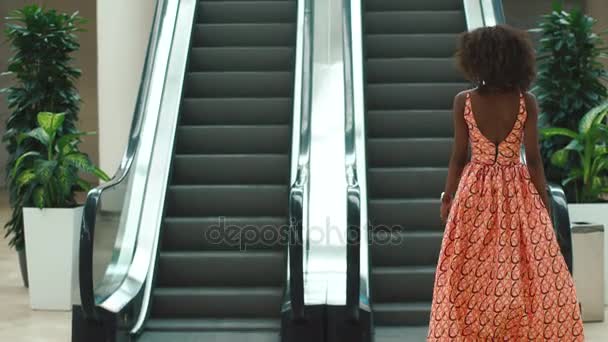 Attractive young african woman in bright orange dress riding the escalator and looking aside — Stock Video