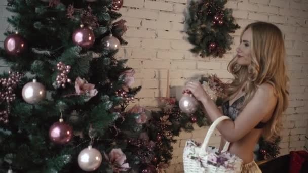 Hermosa chica rubia en lencería sexy está decorando el árbol de Navidad con bolas de plata — Vídeo de stock